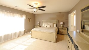 A bedroom with a large bed, bedside tables with lamps, a ceiling fan, and a dresser. - 4 bedroom house close to the Horse Park (Georgetown)