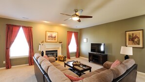 A living room with a sofa, coffee table, fireplace, television, and ceiling fan. - 4 bedroom house close to the Horse Park (Georgetown)