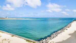 Eine Küstenansicht bei blauem Himmel, ruhigem Meer und einem Sandstrand mit einem Felsenmole.