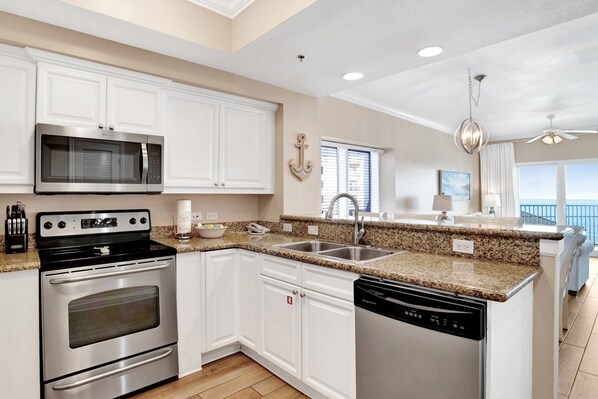 A modern kitchen with white cabinetry, stainless steel appliances, granite countertops, and a view of the ocean.