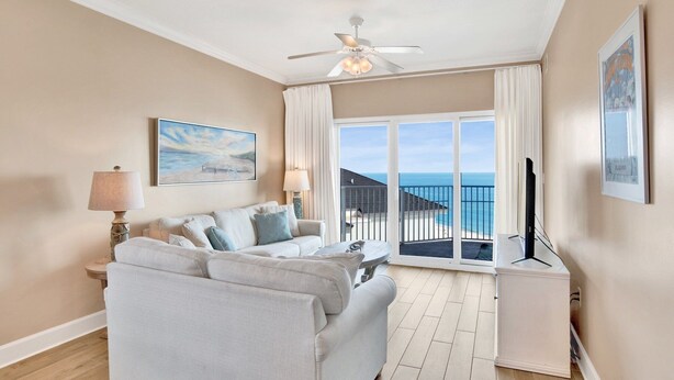 Un soggiorno con divano, una ventola a soffitto, un quadro e vista sull'oceano attraverso ampie finestre.