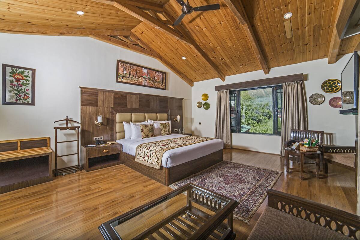 Um quarto espaçoso com uma cama grande, teto de madeira e vista para o verde pela janela.
