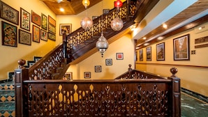 A grand staircase with ornate railings and hanging crystal chandeliers, leading to a second floor with framed artwork on the walls. - Lemon Tree Hotel Srinagar (Srinagar)