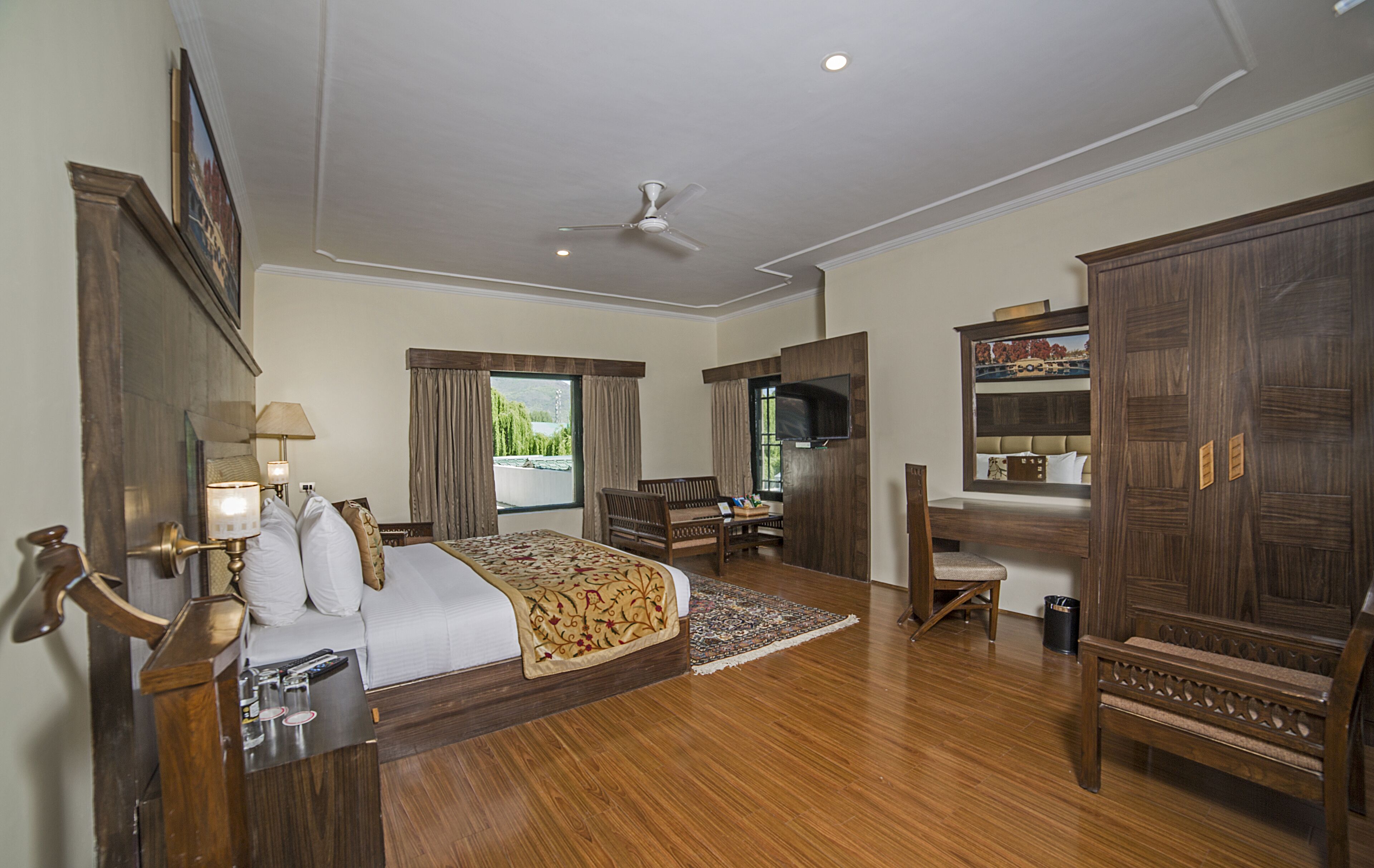 A spacious bedroom with a large bed, a desk, a chair, a wardrobe, and a television.