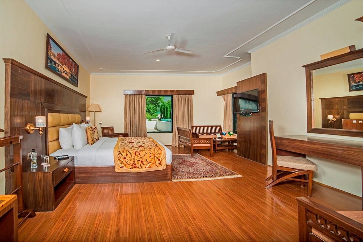Quarto de hotel com cama, escrivaninha, cadeira, televisão e ventoinha no teto.