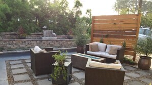 Ein möblierter Patio mit einer Couch, zwei Sesseln und einem Couchtisch. Im Hintergrund sind Kübelpflanzen und eine Steinmauer zu sehen.