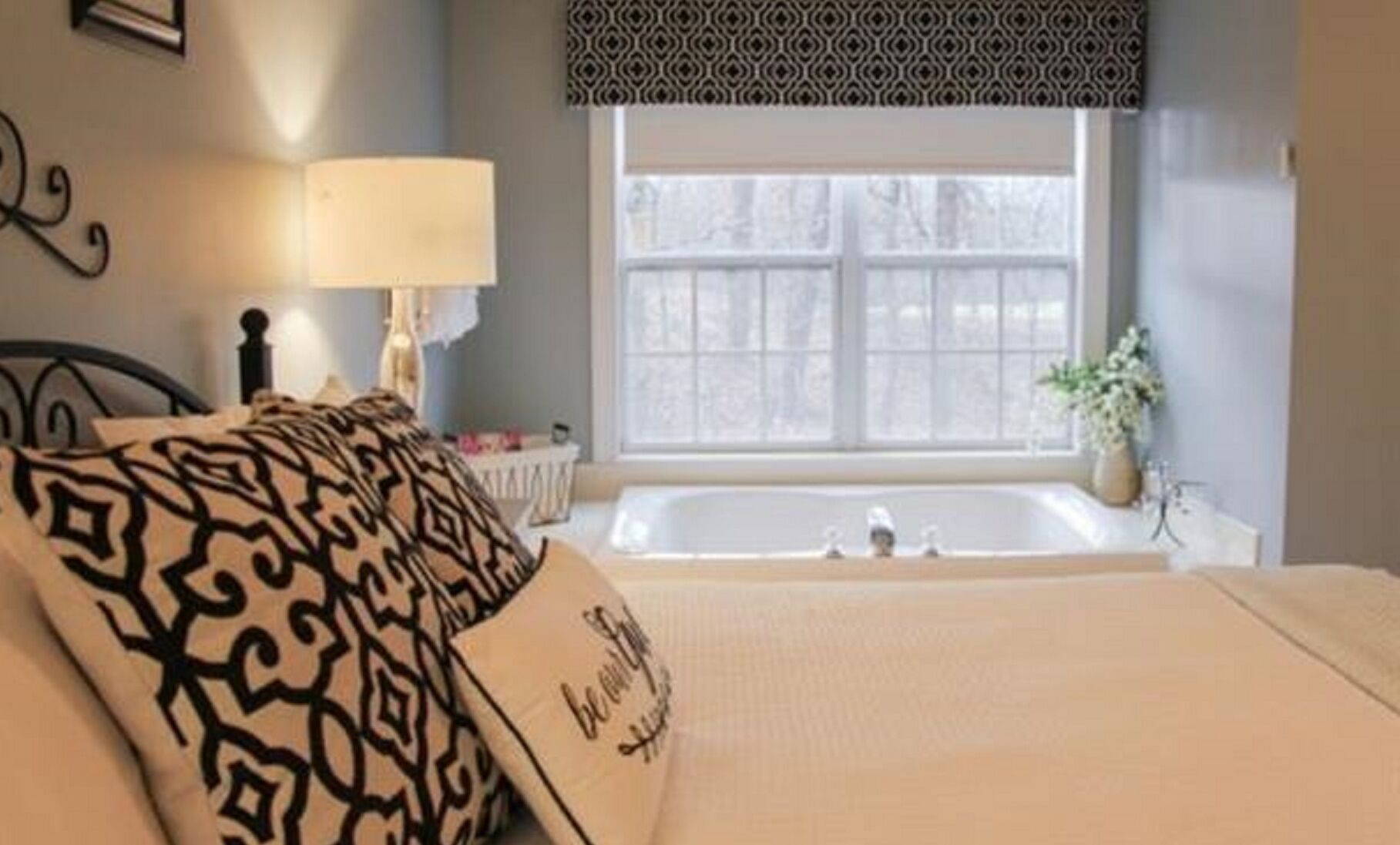 A bedroom with a bed, a window, a lamp, and a bathtub.