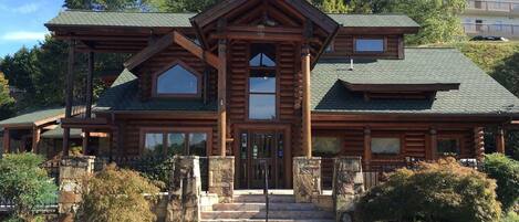A log cabin-style building with a prominent central entrance, stone steps, and a large window above the door.