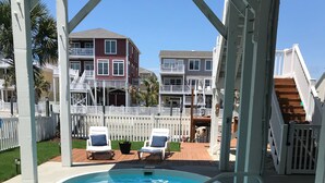 A swimming pool with a white deck, two lounge chairs, and a wooden staircase leading to a deck area.