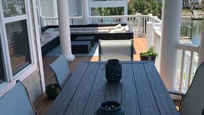 A wooden deck with a table and chairs, a white railing, and a view of a residential area.