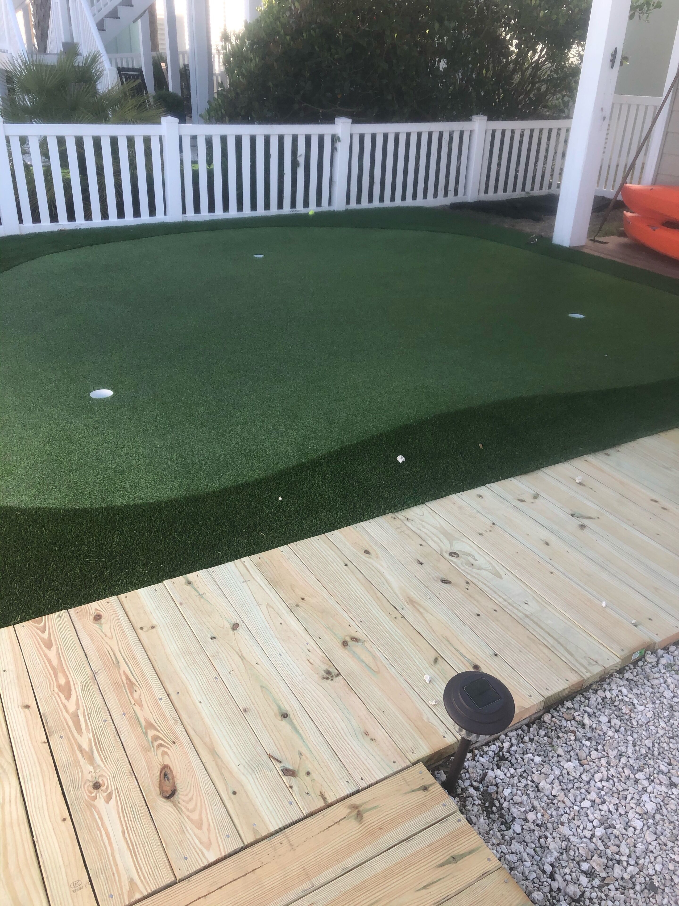 A wooden deck with a green artificial turf area and a white picket fence in the background.