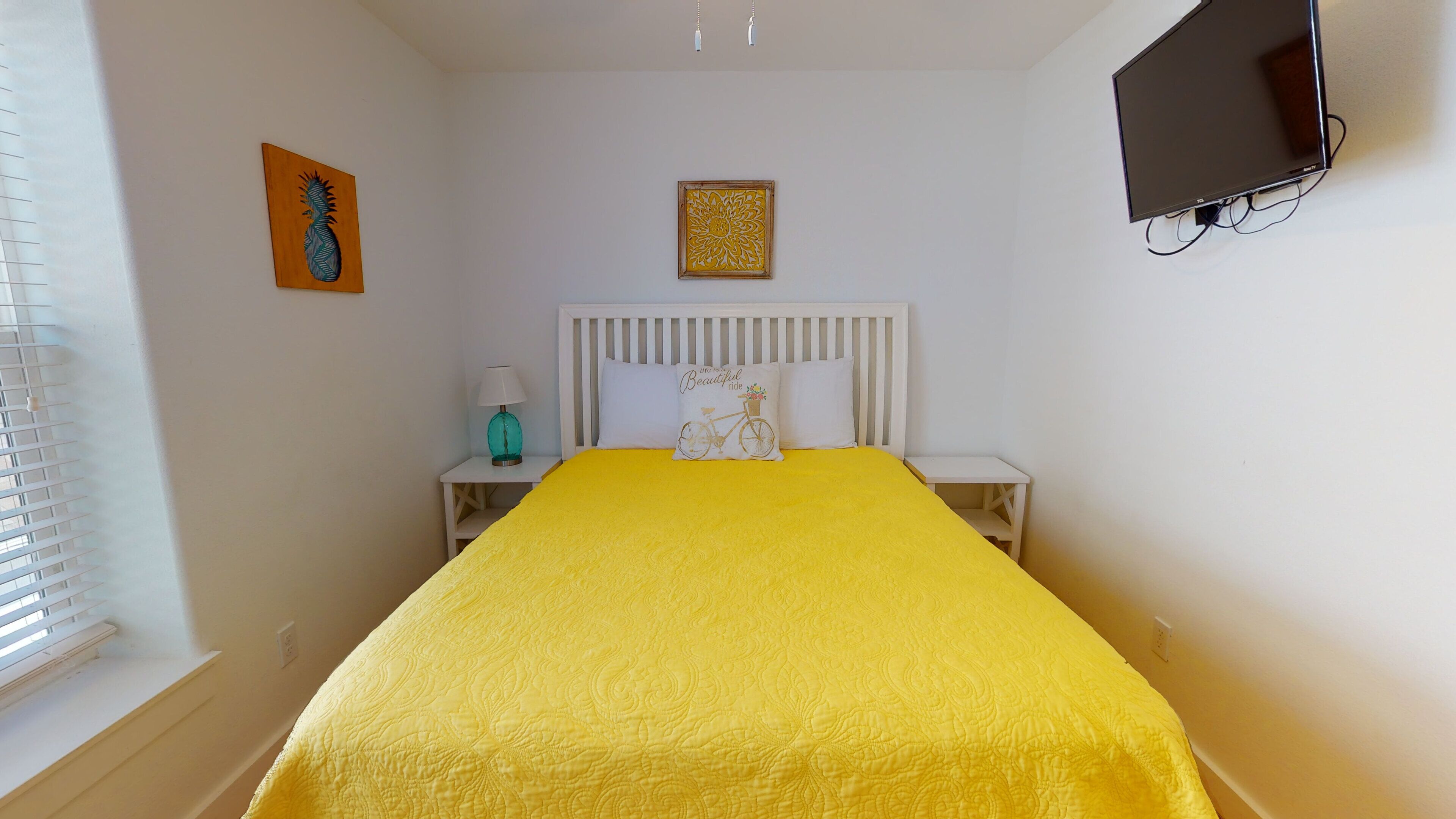 Ein Hotelzimmer mit Bett, Nachttisch, Lampe, Fernseher und Bildern an der Wand.