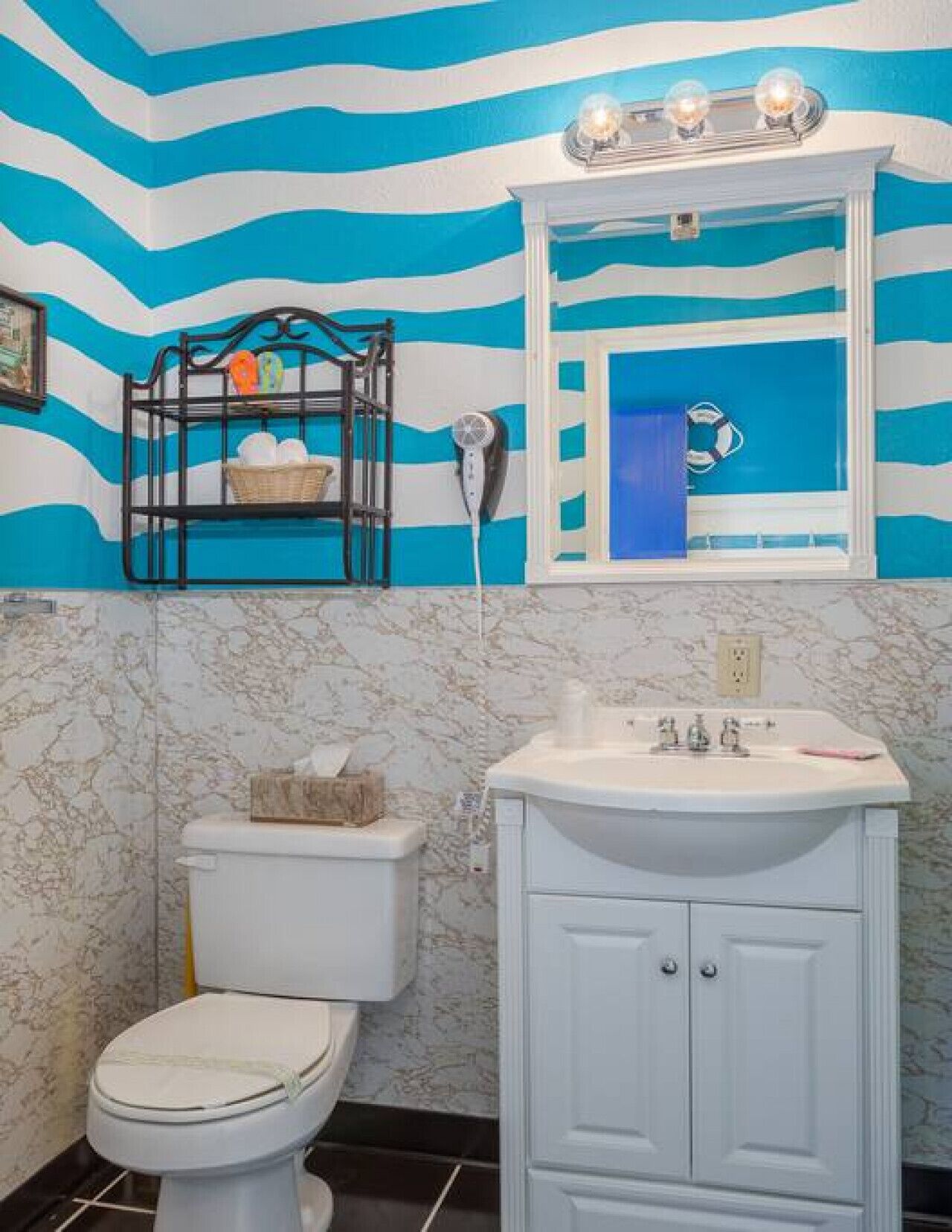 A bathroom with a toilet, sink, and mirror. The walls have a blue and white striped pattern.