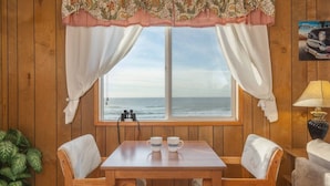 A wooden room with a window overlooking the ocean, a table with chairs, and a lamp. - Moonraker -Oceanfront, balcony, kitchen, fireplace (Lincoln City)