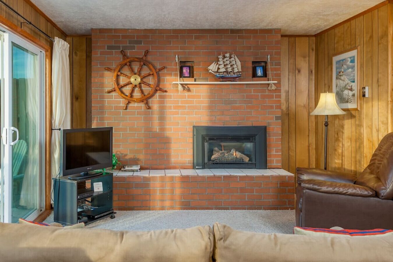 A cozy living room with a brick fireplace, a television, and a leather armchair.