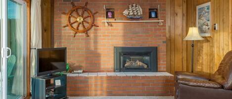 A cozy living room with a brick fireplace, a television, and a leather armchair.