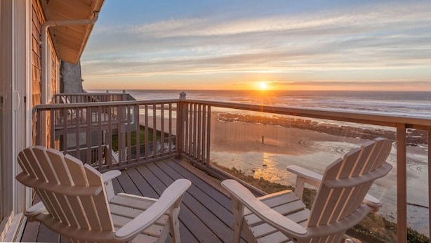A wooden deck with two Adirondack chairs facing a beach at sunset. - Moonraker -Oceanfront, balcony, kitchen, fireplace (Lincoln City)