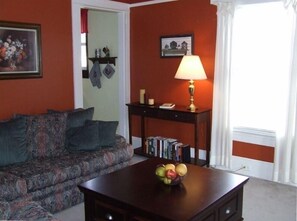 A living room with a sofa, a table with a fruit bowl, a lamp, and a bookshelf. - On 'The New River Trail' (Fries)