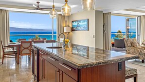 A modern kitchen with a large island, a dining area with chairs, and a view of the ocean.