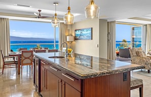 A modern kitchen with a large island, a dining area with chairs, and a view of the ocean.