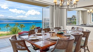 A dining area with a view of the ocean, a chandelier, and a table set for six.