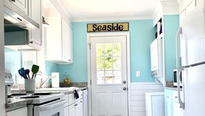 Et køkken med hvide skabe, en komfur og en dør med teksten "Seaside".