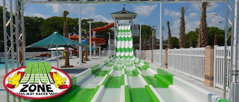 Un parque acuático con un tobogán de agua verde y blanco, otro tobogán de color rojo y un pequeño pabellón.