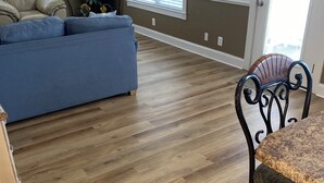 A living room with a blue sofa, a dining table with a chair, and a TV on a stand. - LAKEFRONT, 5 BDRM, Ocean View! Quiet. Fish off deck. Just reduced Aug wks! (Myrtle Beach)