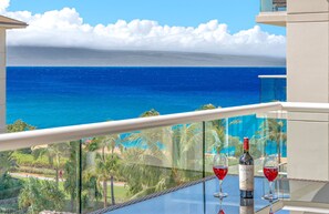 A balcony with a glass railing overlooking a beach and ocean.