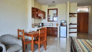 A compact kitchen with wooden cabinets, a dining area with a table and chairs, and a small refrigerator. - Galeodan Bonito Suite - your home In Paradise (Puerto Baquerizo Moreno)