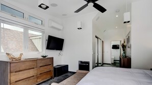 A modern bedroom with a large bed, a wooden dresser, a bench, a flat-screen TV, and a ceiling fan.