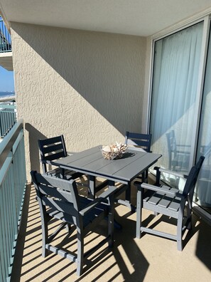 Een balkon met een tafel en stoelen, een klein mandje met schelpen en uitzicht op het strand.