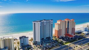 A high-rise hotel with multiple floors, a parking area, and a view of the beach and ocean.
