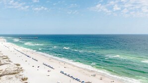 A beach with a long stretch of sand, a pier in the distance, and a clear sky.