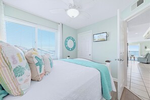 Ein Schlafzimmer mit einem Bett, einem Deckenventilator, einem Fenster mit Jalousien, einer Tür und Blick auf den Balkon.