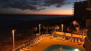 A pool area with lounge chairs and a view of the ocean at dusk.