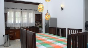 Una cocina con una mesa de comedor, sillas de madera, un refrigerador y una ventana con cortinas.
