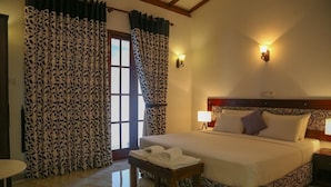 A hotel room with a bed, a nightstand, a table with towels, patterned curtains, and wall sconces. - Sithi Villas (Hikkaduwa)