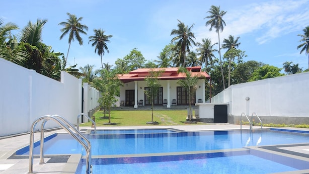 A swimming pool with metal ladders, surrounded by white walls and palm trees. - Sithi Villas (Hikkaduwa)