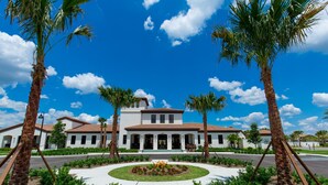 A white building with a tiled roof, surrounded by palm trees and a circular garden.