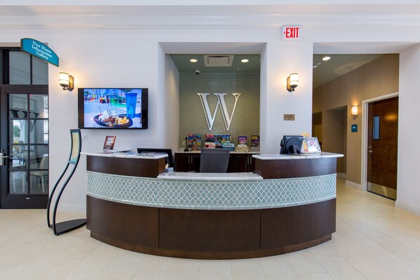 A reception desk with a television displaying a menu, a large 'W' logo, and a sign indicating maximum occupancy.