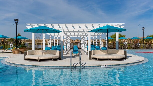A pool area with lounge chairs and umbrellas, a white pergola, and a clear blue sky.