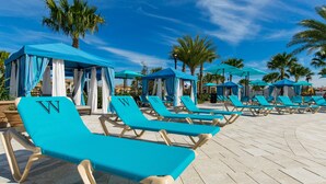 A poolside area with rows of blue lounge chairs and blue canopies.