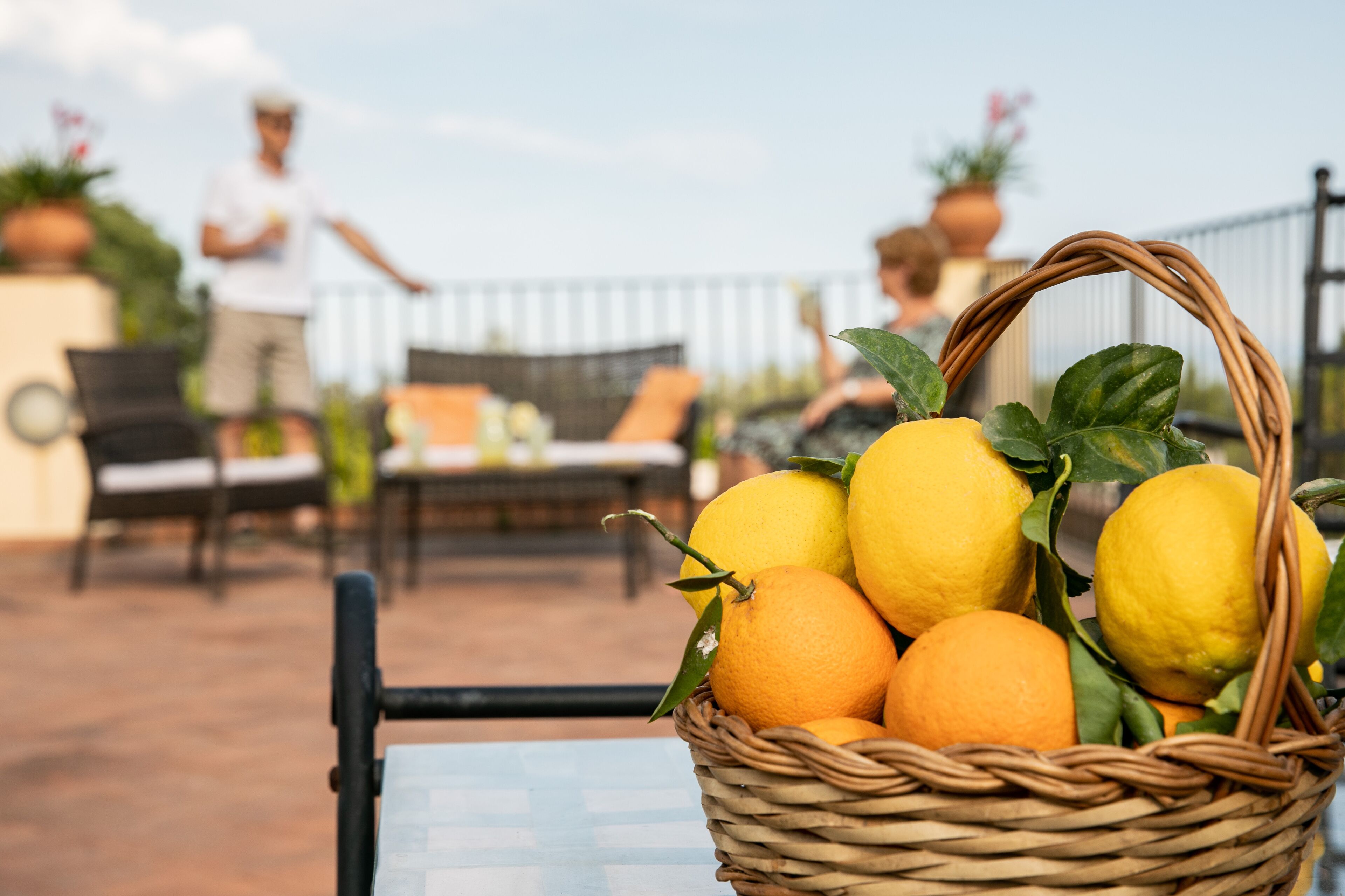 A wicker basket filled with lemons and oranges on an outdoor patio with a table and chairs.