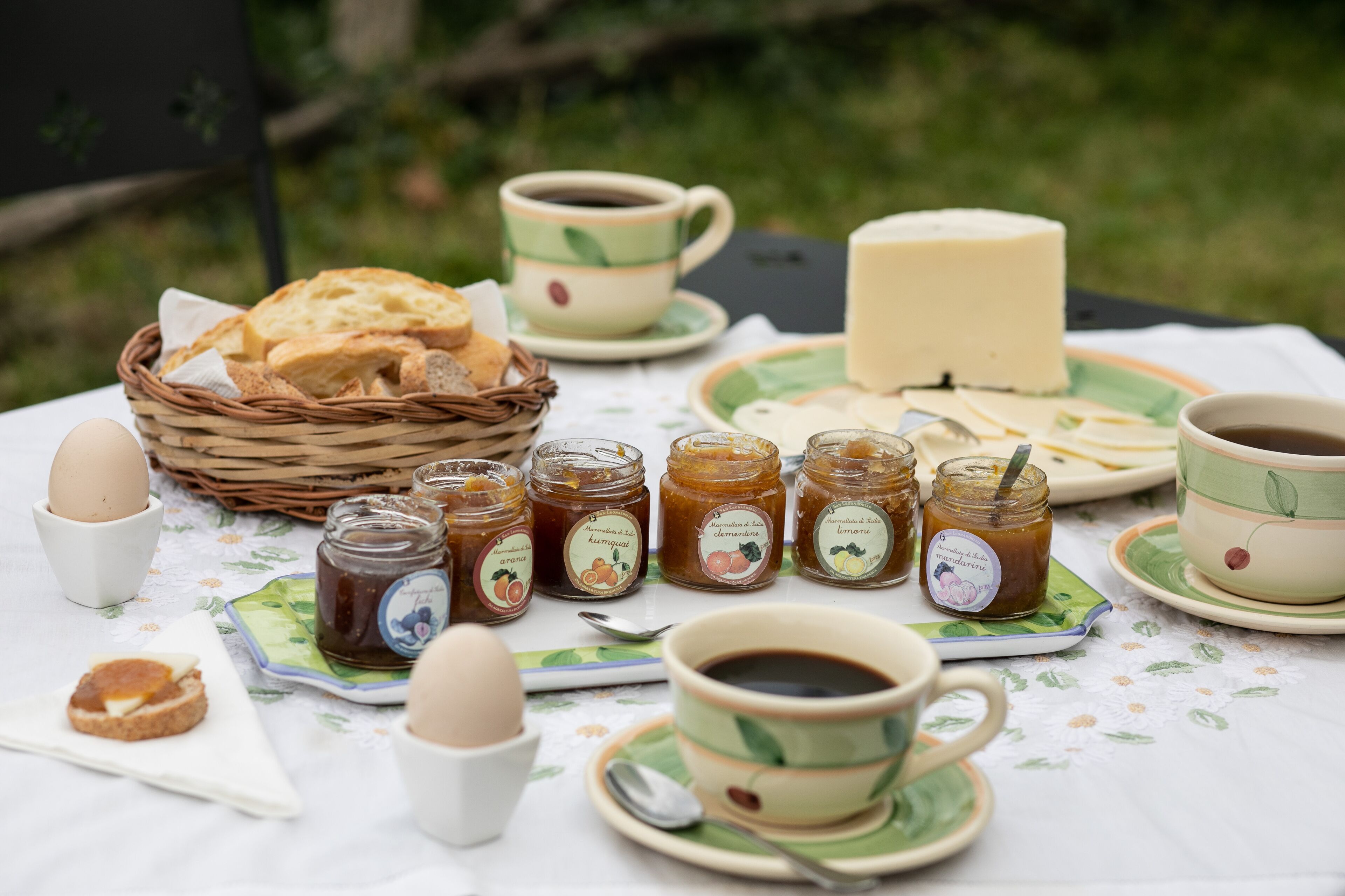 Une table dressée pour un pique-nique avec du pain, du fromage, des œufs et différentes sortes de confitures.