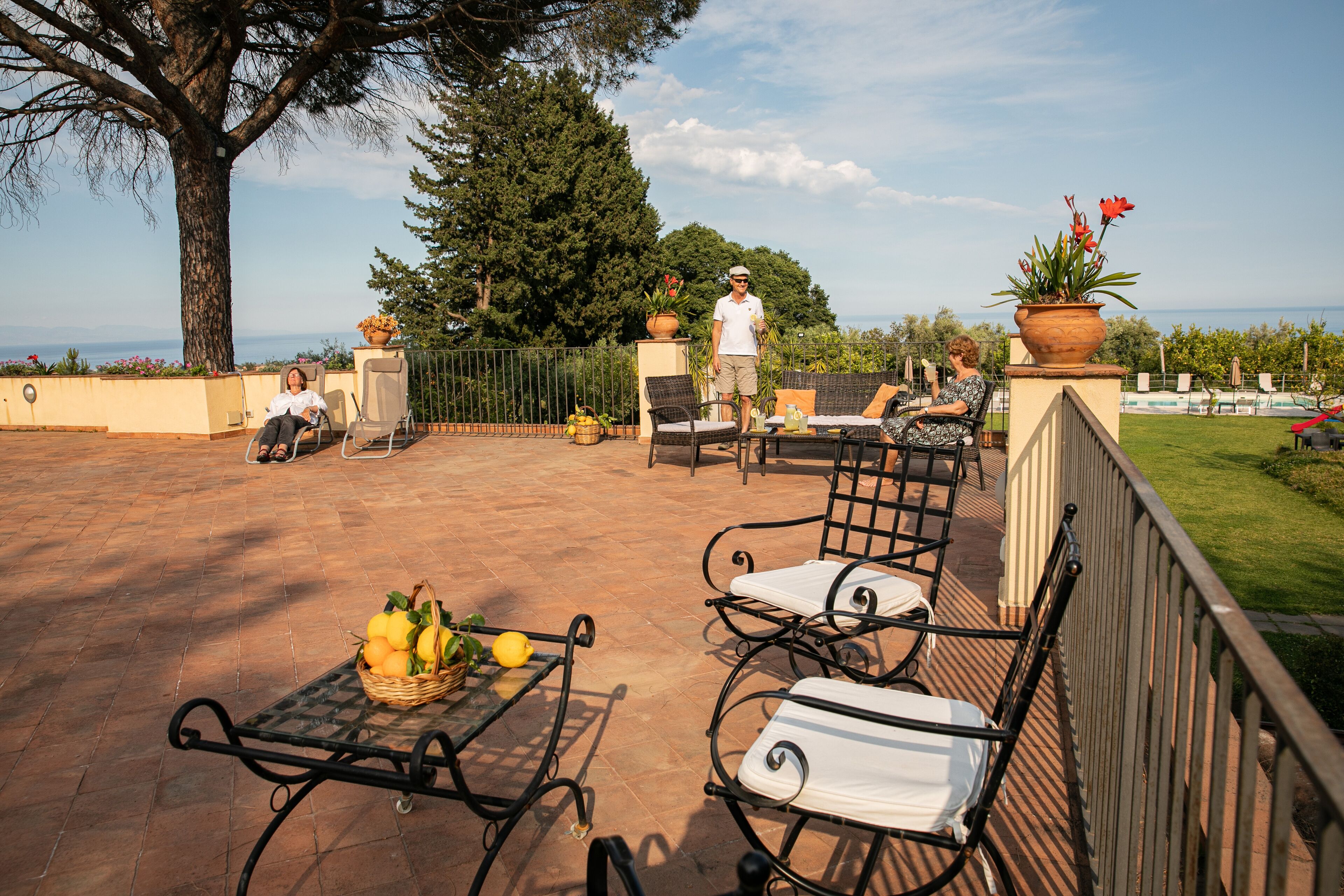 An outdoor patio with wicker furniture, a table with fruits, and a view of the sea.