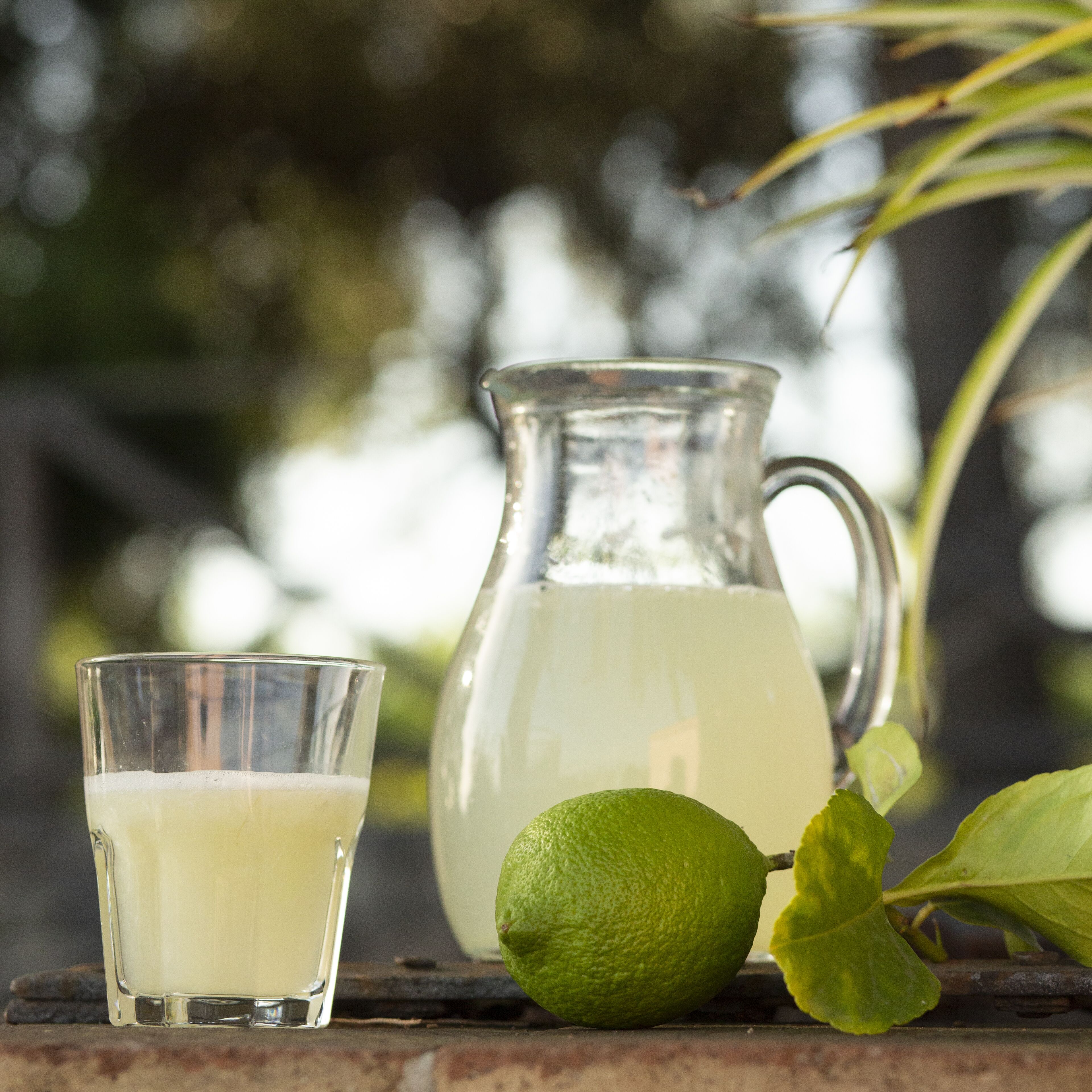 A glass of lemonade, a pitcher, and a lime on a wooden surface.