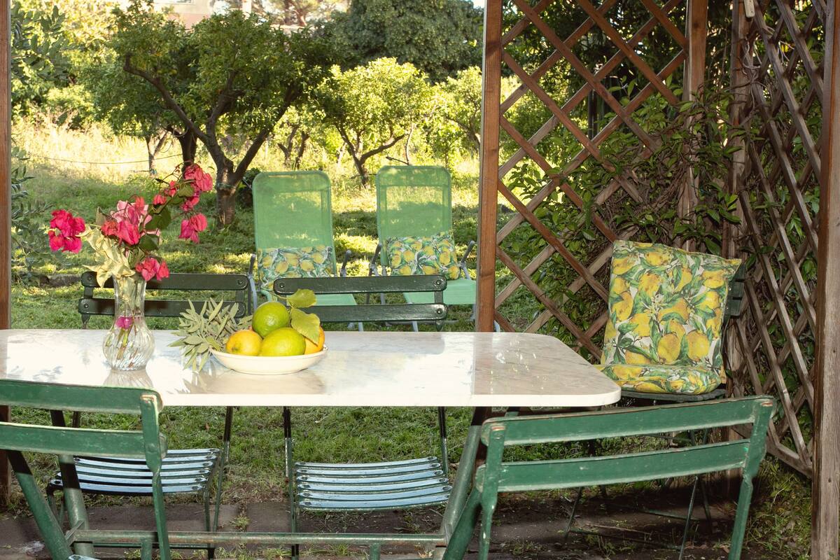 Un jardín al aire libre con una mesa, sillas y un florero con flores.