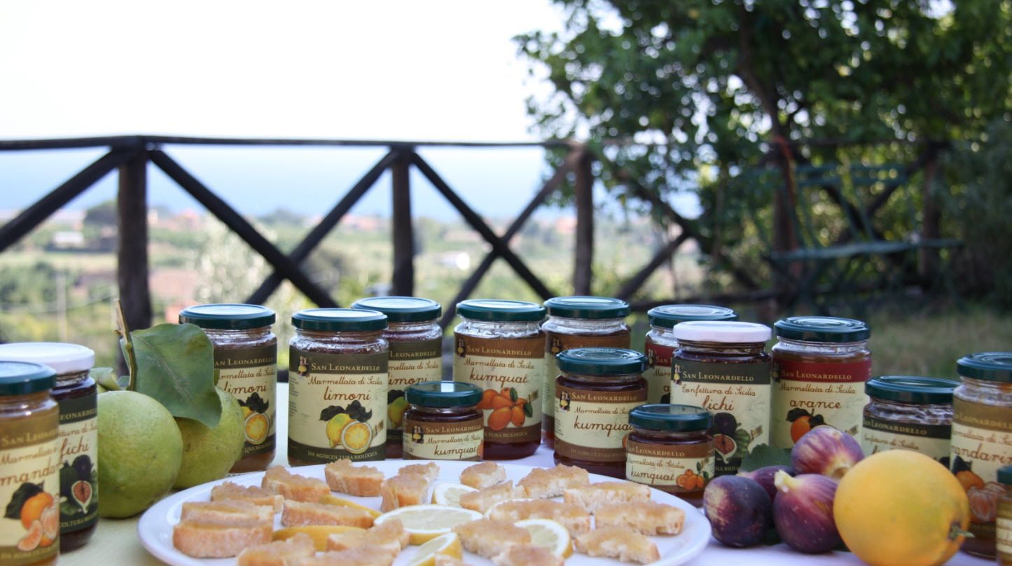 Una mesa con frascos de mermelada San Leonardello de frutas, incluyendo limón, kumquat y ciruela, junto con fruta y repostería.