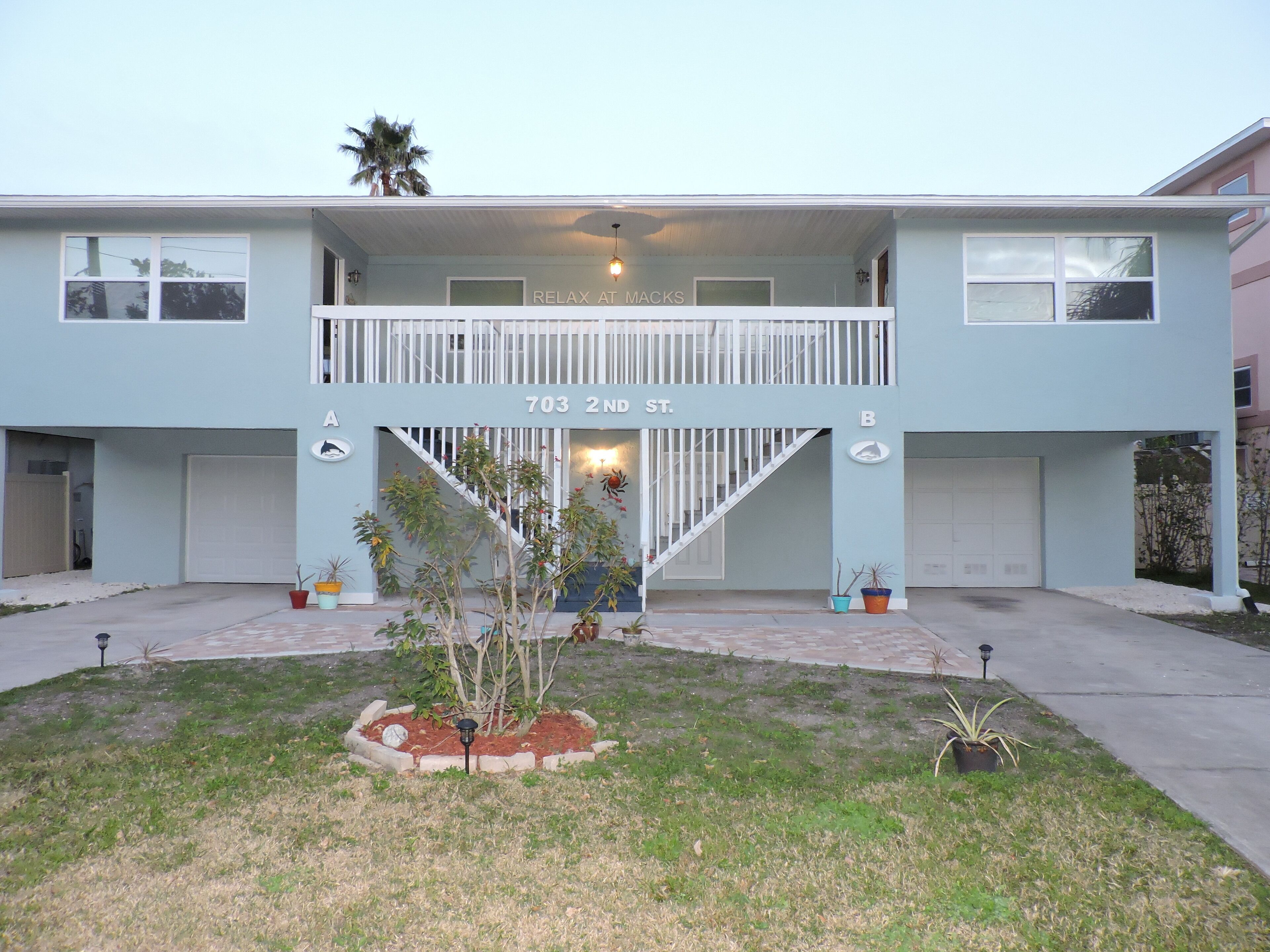 A two-story building with a balcony, a sign reading "703 2ND ST.", and a small garden area with potted plants.